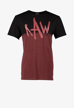 Mann läuft, trägt eine schwarze Kapuzenjacke, ein dunkelbraunes Grafik-T-Shirt, verwaschene blaue Jeans und schwarze Schnürstiefel.
