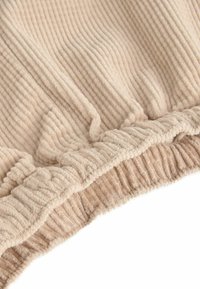 Beige bordázott szövet, textúrált, puha felülettel és fodros szélekkel. Puha és bársonyos megjelenés, amely alkalmas lakberendezéshez vagy textil alkalmazásokhoz.