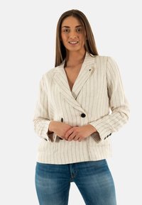 Blazer double boutonnage beige clair avec des rayures verticales bleu marine, revers crantés et deux poches avant. Fabriqué en tissu texturé avec des accents de boutons.