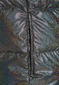 Close-up van glanzende zwarte stof met iriserende stippen en een centrale verticale naad die geplooide vouwen creëert.