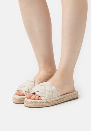 Sandali slip-on beige intrecciati con una tomaia in tessuto intrecciato, suola in juta e design open-toe, che offrono una finitura naturale e testurizzata.