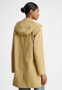 Béžový kapucňový kabát s elegantným dizajnom, vyrobený z ľahkej látky. Má zadný rozparok a dlhé rukávy.