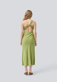 Grön, satin midi klänning med en vriden ryggstroppdesign, öppen rygg och slät textur. Har en rundad halsringning och rak nederkant.