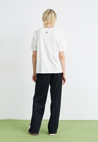 T-shirt en coton blanc avec un logo Jordan noir au dos, associé à un pantalon noir. Texture lisse et coupe décontractée.