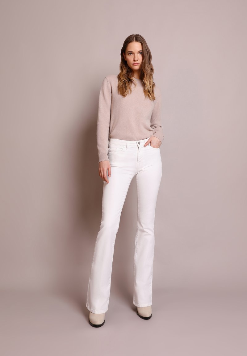 Suéter beige combinado con jeans acampanados blancos. Los jeans cuentan con un diseño clásico de cinco bolsillos y detalles de costura sutiles.