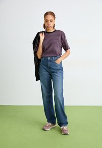 Maglietta a righe a maniche corte in blu navy e bordeaux, jeans blu a vita alta, sneaker casual e una giacca nera gettata su una spalla.