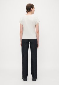 Hvit topp med korte ermer, rullet ermer og bakseam, paret med svarte straight-leg jeans, sett fra baksiden.