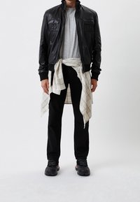 Czarna skórzana kurtka z dwiema kieszeniami na piersi, szary T-shirt, czarne spodnie i koszula w kratę zawiązana w pasie. Czarnym sneakersy dopełniają całość.