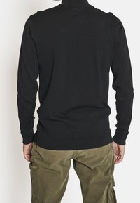 Musta pitkähihaine neule, jossa on ribbitekstuuri, tiukat hihansuut ja korkea kaulus, yhdistettyinä oliivinvihreisiin cargo-housuihin, joissa on sivutaskut.