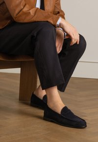 Marineblaue Wildleder Slipper mit einer strukturierten Oberfläche, ausgestattet mit einer flachen Sohle und einer gesteppten Akzentnaht auf dem Vorderblatt, kombiniert mit schwarzen maßgeschneiderten Hosen.