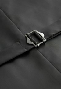 Un tissu noir au toucher lisse présente une boucle en métal argenté avec des extrémités circulaires. Le tissu est soigneusement plié et cousu.