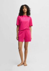 Ljust rosa bomull t-shirt och matchande shorts med elastisk midja. T-shirten har en liten logotyp på framsidan. Slät textur.