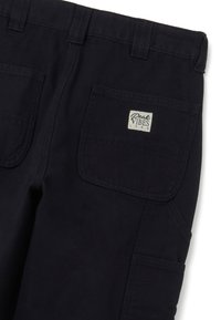 Marineblaue Baumwollhose mit geradem Bein, zwei Gesäßtaschen, einem kleinen Etikett mit der Aufschrift "Peak Vibes" und Ziernähten.