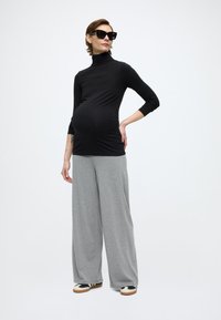 Μαύρο εφαρμοστό τοπ ζιβάγκο με μακριά μανίκια, συνδυασμένο με άνετο γκρι παντελόνι χαλάρωσης, φορεμένο με μαύρα γυαλιά ηλίου και παπούτσια με σχέδιο.