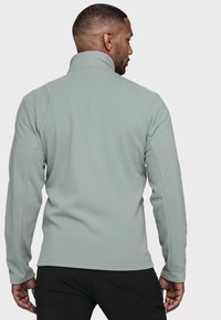 Helle graue Fleecejacke mit hohem Kragen, langen Ärmeln und glatter Textur. Verfügt über ein figurbetontes Design und Nahtakzente.