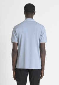 Polo shirt bleu clair à manches courtes, avec un col plat et des accents blancs sur les manches. Texture simple et lisse.