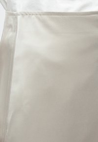 Φούστα σε ανοιχτό μπεζ χρώμα με απαλό, ελαφρώς υφασμένο ύφασμα. Διαθέτει ραφή στο πλάι, που δημιουργεί μια καθαρή, καλοραμμένη σιλουέτα.