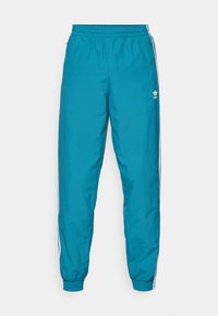 Pantaloni da jogging Adidas turchesi con elastico in vita e alle caviglie, strisce laterali bianche e logo Adidas sulla coscia sinistra.