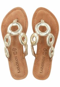 Sandales plates avec une semelle en cuir tanné, des accents de chaîne métallique dorée et un design avec un séparateur de orteils. L'intérieur présente un logo en relief.