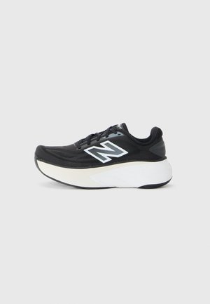 Zapatilla de correr New Balance en blanco y negro con suela gruesa, logo lateral y cierre de cordones sobre un fondo gris liso.