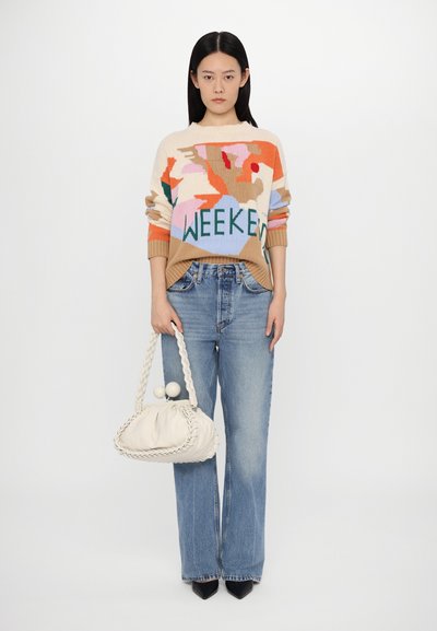 Beige tröja med färgglada abstrakta mönster och texten "WEEKEND", tillsammans med ljusblå utställda jeans och en krämfärgad handväska med flätade detaljer.