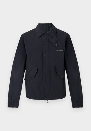 Μαύρο ελαφρύ μπουφάν με μπροστινά κουμπιά με πατιλέτα, δύο τσέπες με καπάκι, ελαστικές μανσέτες και μικρό λογότυπο "Armani Exchange" στο στήθος.