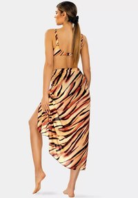 Dwuczęściowy strój kąpielowy z wzorem pasków tygrysa w ciepłych odcieniach. Góra ma szerokie ramiączka, a spódnica o kroju high-low posiada boczne rozcięcie.
