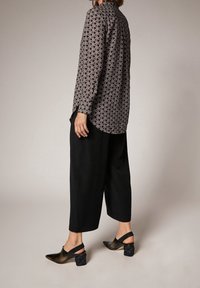 Chemise à manches longues à motifs géométriques dans des tons foncés ; associée à un pantalon noir ample et des chaussures à talons ouvertes à l'arrière.