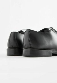 Czarne skórzane buty o gładkiej fakturze, okrągłym nosku i pięcie z zakładką z gumy. Charakteryzują się minimalnym szyciem i klasycznym sznurówkowym zapięciem.