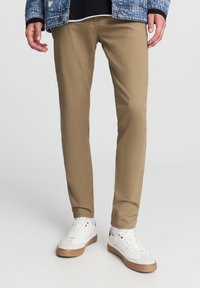 Beżowe chinosy o prostym kroju, wykonane z bawełnianego materiału. Noszone z białymi trampkami z gumową podeszwą i czarnymi akcentami.