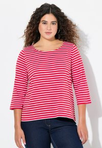Rot-weiß gestreiftes Shirt mit Dreiviertelärmeln, Rundhalsausschnitt, aus weichem Baumwollmaterial, kombiniert mit dunkelblauen Jeans.