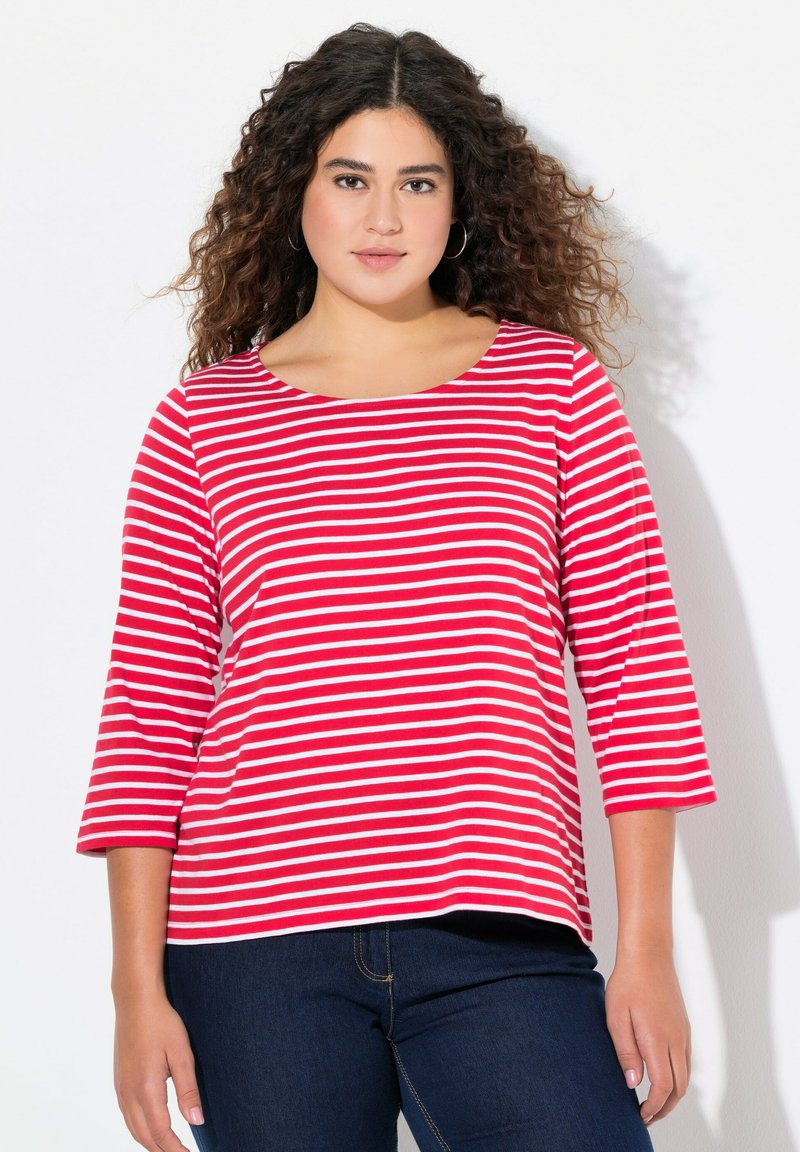 Maglietta a righe rosse e bianche con maniche a tre quarti, scollatura rotonda, materiale in cotone morbido, abbinata a jeans in denim blu scuro.