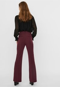 Bordeauxkleurige flared broeken met een hoge taille, nauwkeurige stikdetails en een gladde stofafwerking. Achterzakken zijn zichtbaar.