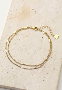 Pulsera de oro con capas y eslabones texturizados, que cuenta con un cierre de langosta y una cadena de extensión, exhibida sobre una superficie de piedra de color claro.