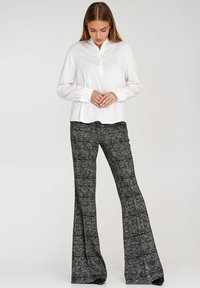 Biała koszula z długim rękawem i kołnierzykiem, zestawiona z czarno-białymi, teksturowanymi spodniami dzwonami, z delikatnym wzorem i luźnym krojem.