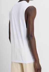 Débardeur blanc sans manches avec un col rond, texture lisse et détails de couture, vu de dos. Tissu léger qui tombe doucement.