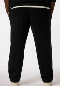 Sorte svedbukser med elastisk talje og sidelommer, samt en tapered ben design. Stoffet ser blødt og glat ud.