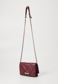 Burgundy quilted faux leather crossbody bag with a gold-tone chain strap and logo accent on the front. Compact rectangular shape.