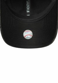 Gorra negra con visera curvada, que presenta una etiqueta blanca de béisbol en la parte inferior. El material es tela texturizada, con detalles de costura.