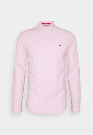 Camisa de manga larga rosa claro hecha de algodón, con un cuello clásico, cierre de botones en la parte delantera y un pequeño logo en el pecho. Textura suave.