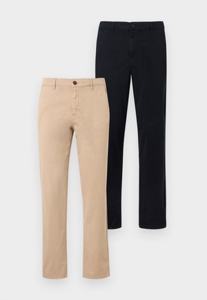 Άνδρας που στέκεται φορώντας ένα ανοιχτομπλε ριγωτό πουκάμισο με μακριά μανίκια, μαύρο παντελόνι και μαύρα αθλητικά παπούτσια με λευκή σόλα.