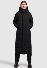 Cappotto piumino lungo nero con collo alto, tasche con zip e design trapuntato. Presenta una vestibilità dritta e accenti minimalisti.