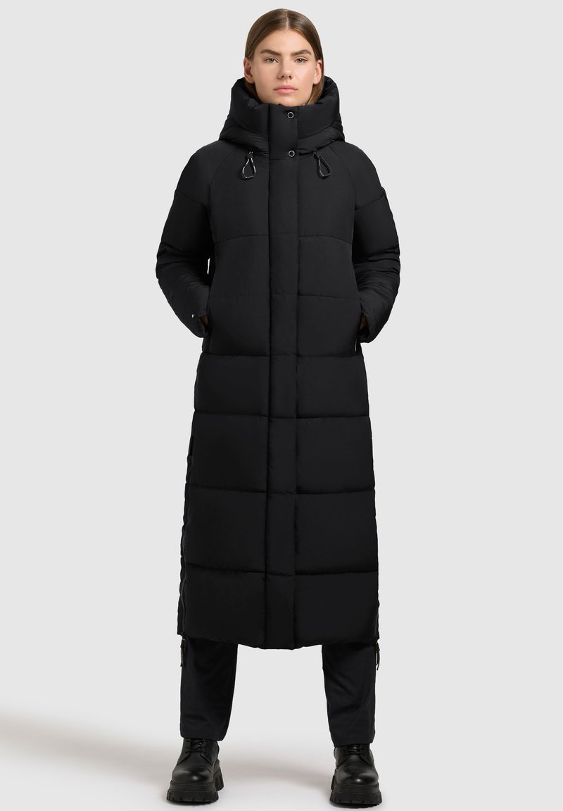 Cappotto piumino lungo nero con collo alto, tasche con zip e design trapuntato. Presenta una vestibilità dritta e accenti minimalisti.