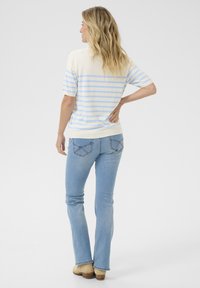 Pull rayé crème et bleu clair, à manches courtes, associé à un jean bleu clair et des chaussures beige, vu de dos.