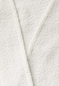 Vit texturerad tyg med ett vågigt mönster, som har en mjuk, ludig yta. Materialet har en svag lyster och är vikt diagonalt.