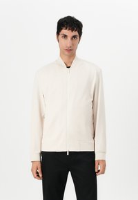 Light beige bomber jacket with a stand-up collar, front zipper closure, and two side pockets. Smooth texture with ribbed cuffs and hem.