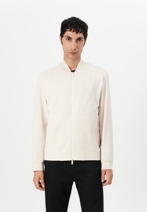 Ljust beige bomberjacka med ståkrage, frontdragkedja och två sidofickor. Slät textur med ribbad muddar och nederkant.