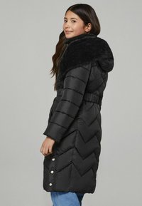 Cappotto piumino nero con colletto in pelliccia sintetica, caratterizzato da un design a rombi trapuntato, vita elastica e dettagli con bottoni a pressione sui lati.