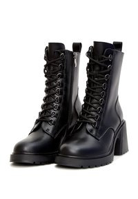 Bottines en cuir noir avec un talon épais, équipées d'un laçage à l'avant, d'une fermeture éclair sur le côté et d'une semelle en caoutchouc texturée pour une meilleure adhérence.