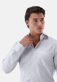 Camicia bianca con bottoni, caratterizzata da un motivo a quadri blu, colletto strutturato e maniche lunghe con chiusura a bottoni. Tessuto morbido.